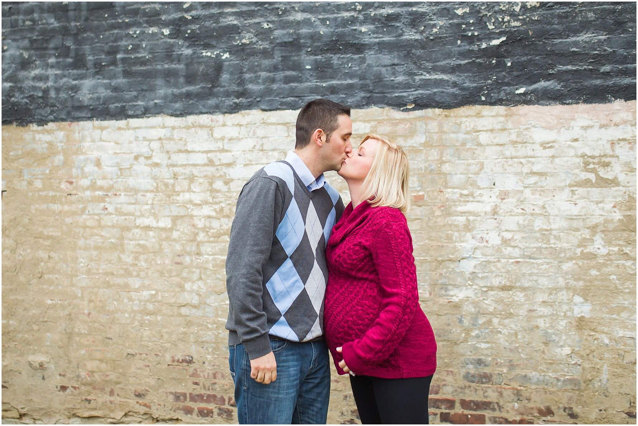 pittsburgh maternity portrait session jaclyn and thomas, kissing in front of a tall brick wall in pittsburgh.
